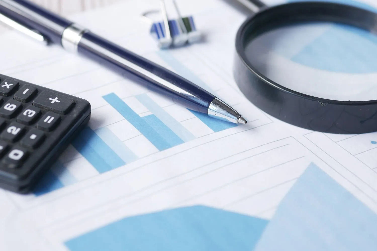 Caneta, calculadora, clipes e lupa sobre documentos impressos com gráficos financeiros