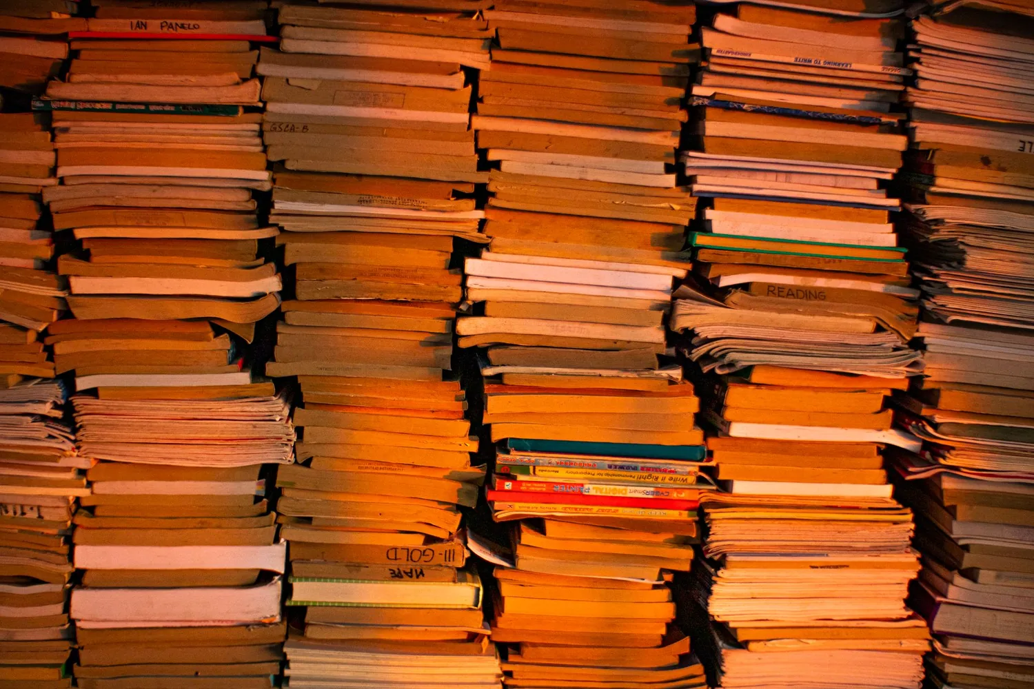 Estante com livros empilhados e um caderno de anotações aberto ao lado