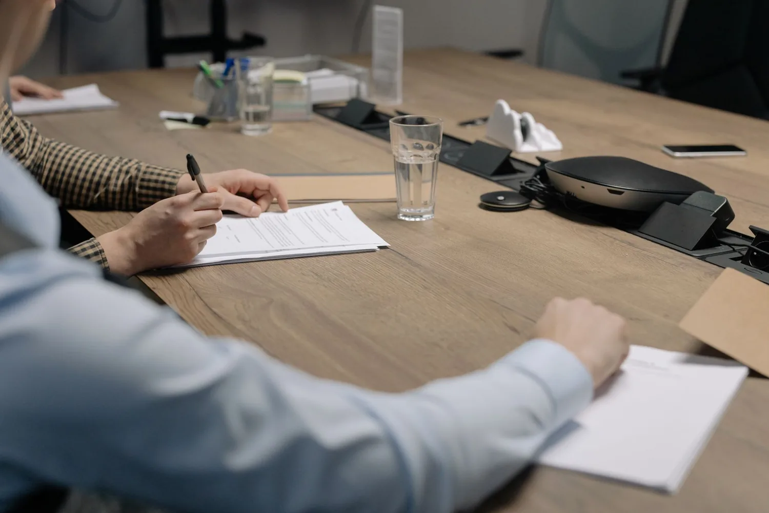 Duas pessoas revisando cláusulas de contrato em uma mesa de reunião, de frente uma para a outra
